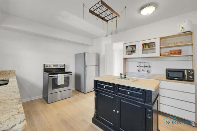kitchen featuring a kitchen island, open shelves, dark cabinetry, stainless steel appliances, and light wood-style flooring