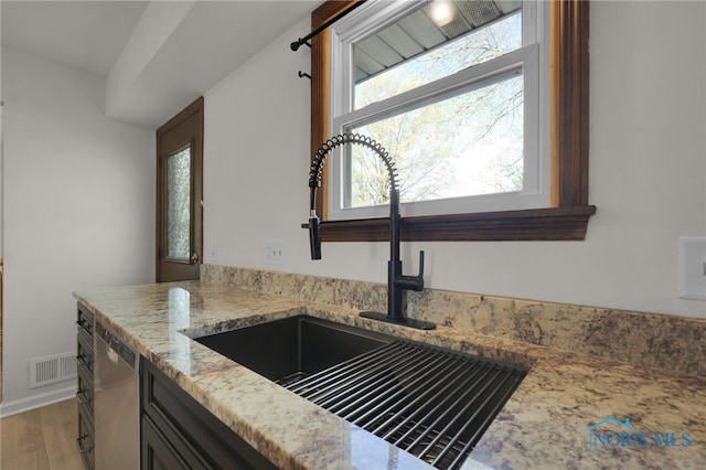 interior details with stainless steel dishwasher, visible vents, light stone countertops, a sink, and light wood finished floors