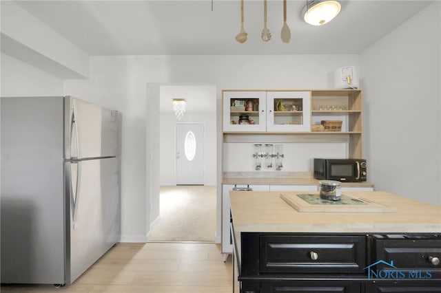 kitchen featuring black microwave, dark cabinets, butcher block countertops, freestanding refrigerator, and light wood-type flooring