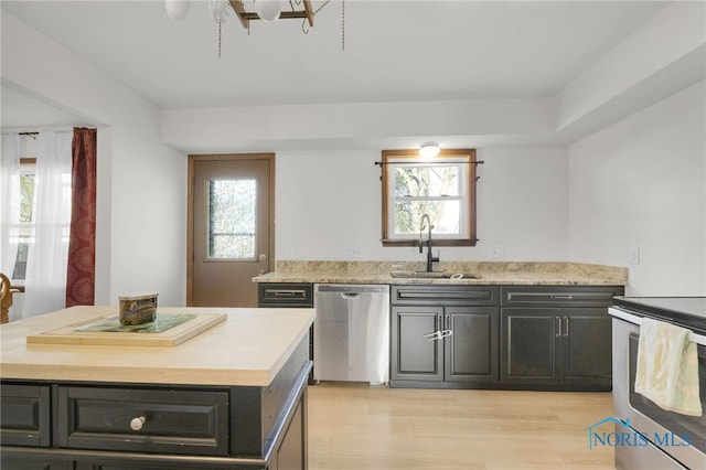 kitchen with light wood-type flooring, a center island, light countertops, a sink, and appliances with stainless steel finishes