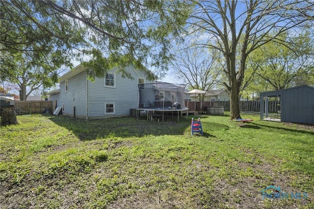 view of yard with a fenced backyard, a storage unit, a trampoline, and an outbuilding