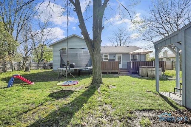 view of yard featuring a deck, a fenced backyard, and a trampoline