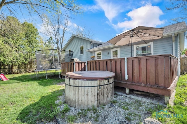 exterior space featuring a yard, a hot tub, fence, and a trampoline