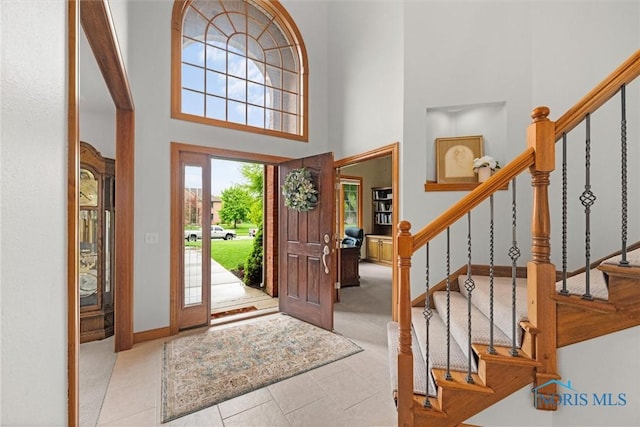 tiled foyer entrance with stairs, a high ceiling, and baseboards