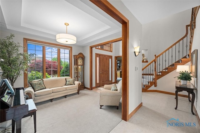 living area featuring stairs, baseboards, a tray ceiling, and light tile patterned flooring