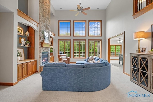 living room with ceiling fan, light carpet, a fireplace, a towering ceiling, and baseboards