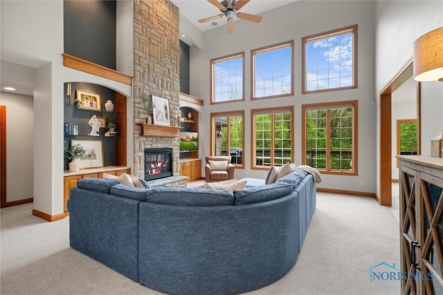 living room with a fireplace, a towering ceiling, light colored carpet, baseboards, and ceiling fan