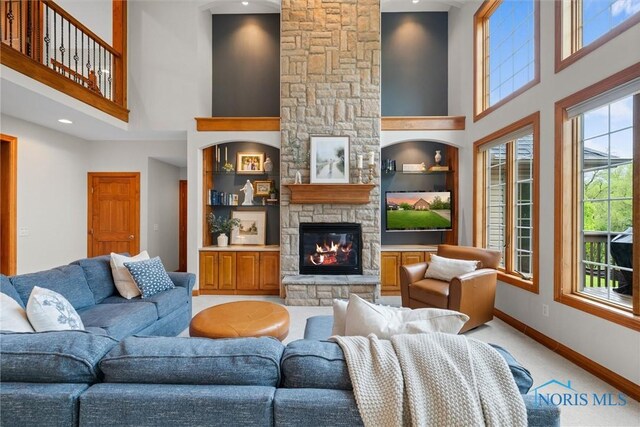 living room with a towering ceiling, a stone fireplace, baseboards, light colored carpet, and built in features