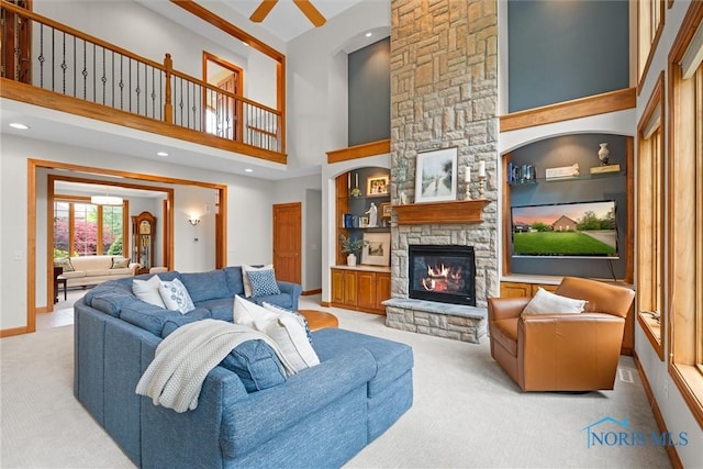 living area with light colored carpet, a stone fireplace, a towering ceiling, a ceiling fan, and baseboards
