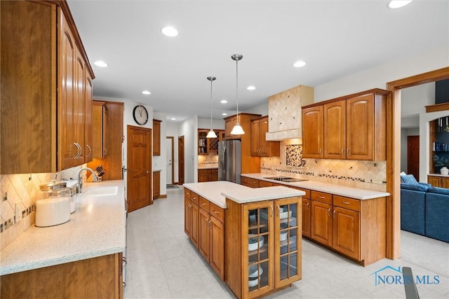 kitchen featuring freestanding refrigerator, black electric cooktop, a sink, brown cabinetry, and glass insert cabinets