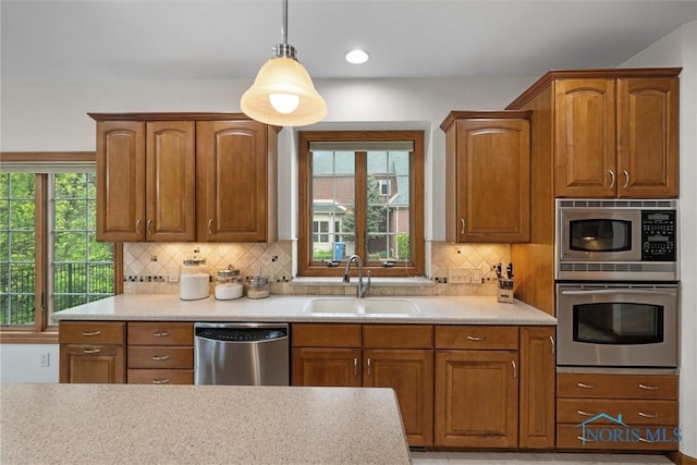 kitchen featuring stainless steel appliances, a sink, light countertops, hanging light fixtures, and backsplash