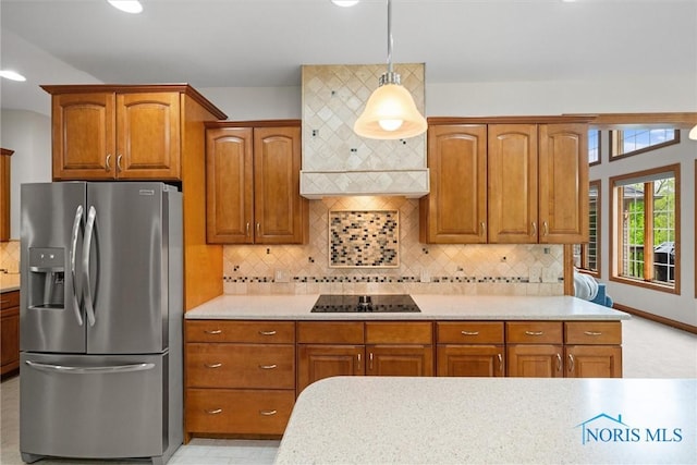 kitchen featuring stainless steel refrigerator with ice dispenser, light countertops, black electric stovetop, hanging light fixtures, and brown cabinetry