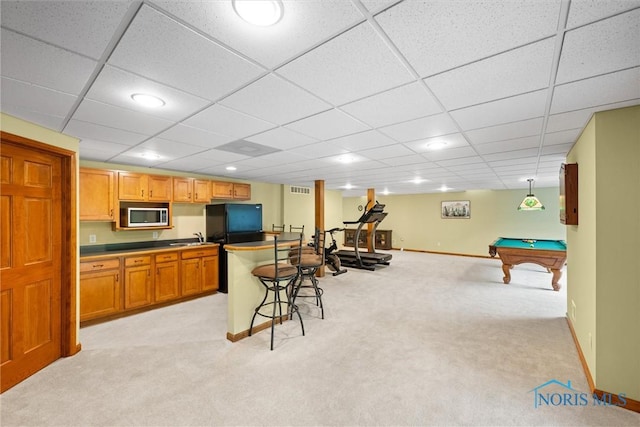 kitchen featuring stainless steel microwave, baseboards, light colored carpet, a kitchen bar, and a drop ceiling