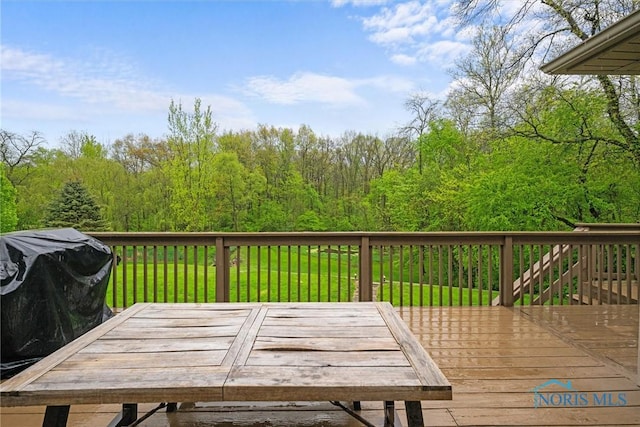 wooden deck featuring a forest view, outdoor dining area, and a lawn