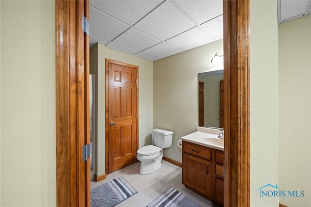 bathroom featuring toilet, a drop ceiling, vanity, and baseboards