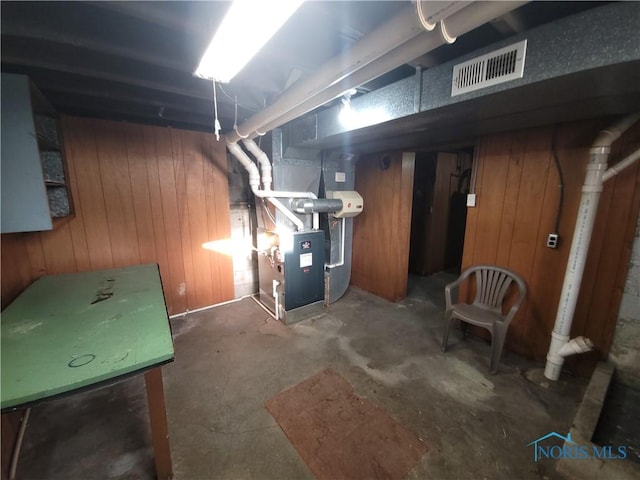 unfinished basement featuring heating unit, visible vents, and wood walls