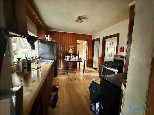 kitchen featuring a sink, gas range, wooden walls, light wood-type flooring, and refrigerator
