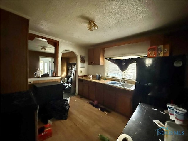 kitchen with a sink, arched walkways, light wood-style flooring, a textured ceiling, and freestanding refrigerator