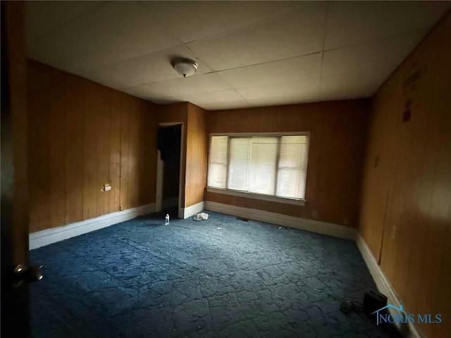 unfurnished room featuring baseboards, dark carpet, and wooden walls