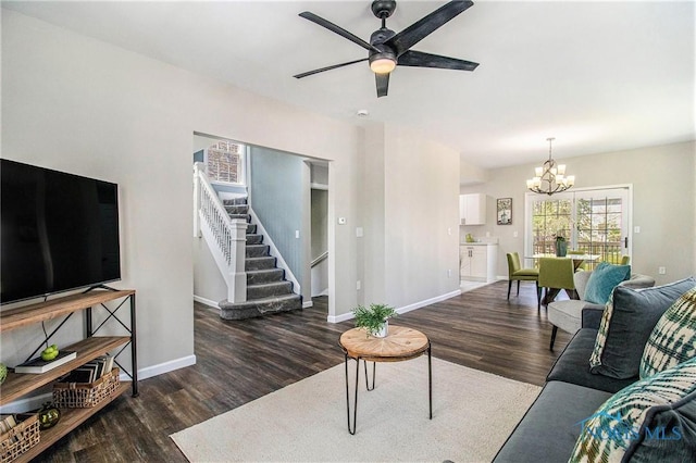 living area featuring wood finished floors, baseboards, ceiling fan with notable chandelier, and stairs