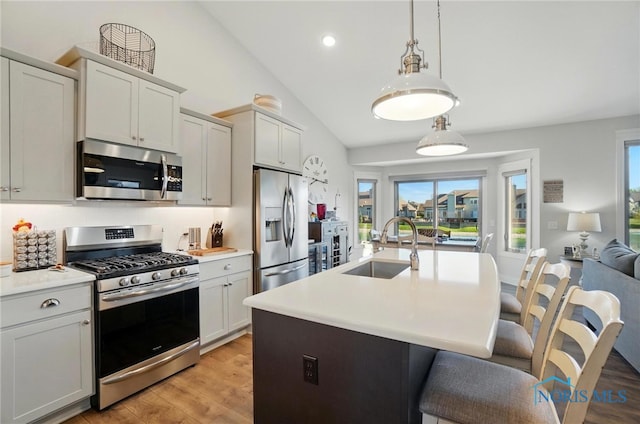 kitchen featuring light countertops, a sink, light wood finished floors, vaulted ceiling, and stainless steel appliances