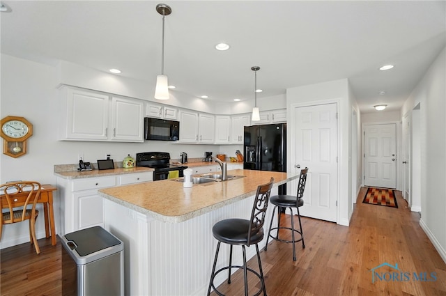 kitchen featuring light countertops, black appliances, light wood finished floors, a sink, and white cabinetry