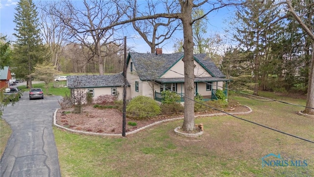view of front of house featuring a chimney, aphalt driveway, and a front lawn