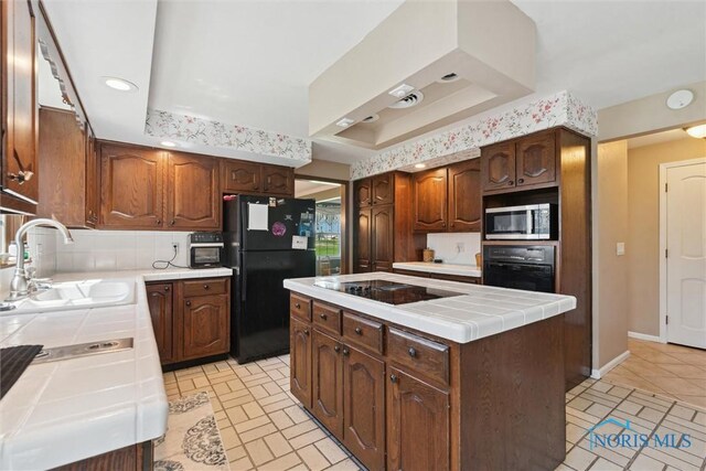 124 Miller Ave, Archbold, OH 43502 - kitchen featuring tile counters, black appliances, a sink, a raised ceiling, and a center island