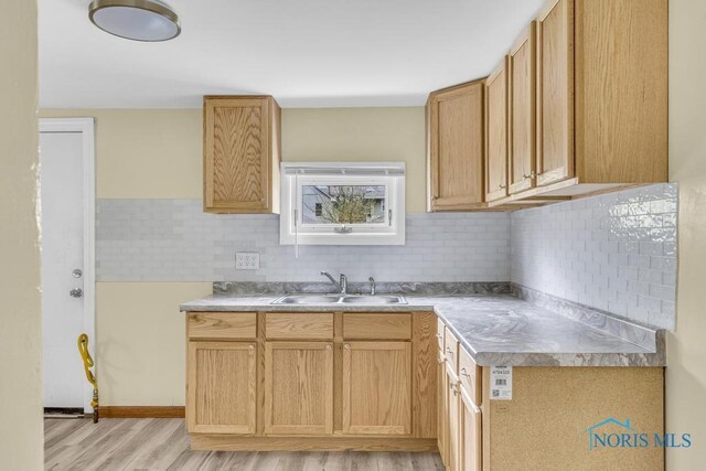 kitchen featuring light countertops, tasteful backsplash, a sink, and light wood-type flooring