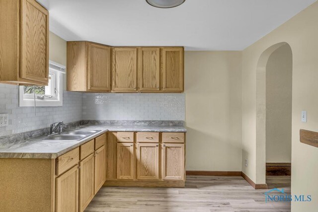 kitchen featuring decorative backsplash, light wood-type flooring, light countertops, arched walkways, and a sink