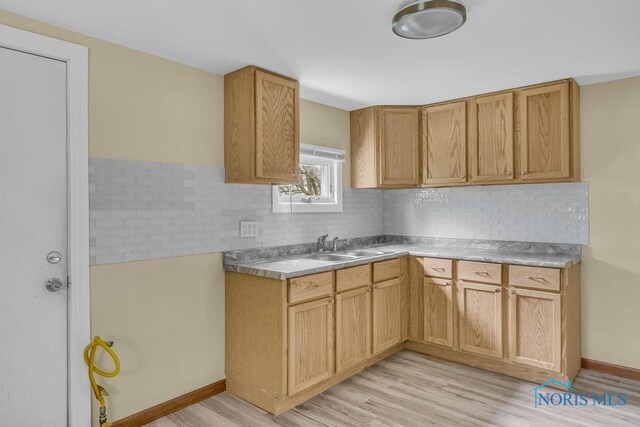 kitchen featuring backsplash, light wood-type flooring, a sink, light countertops, and baseboards