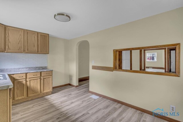 kitchen featuring light countertops, arched walkways, baseboards, and light wood finished floors
