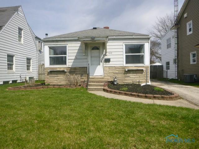 bungalow-style house with a front lawn, central air condition unit, stone siding, and entry steps