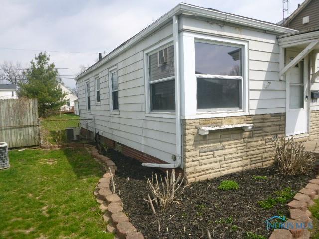 view of home's exterior featuring a lawn, fence, central air condition unit, and stone siding