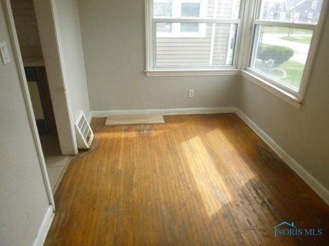 spare room featuring baseboards, visible vents, and wood finished floors