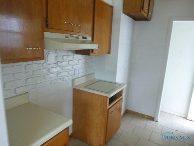 kitchen with backsplash, under cabinet range hood, light countertops, and brown cabinets