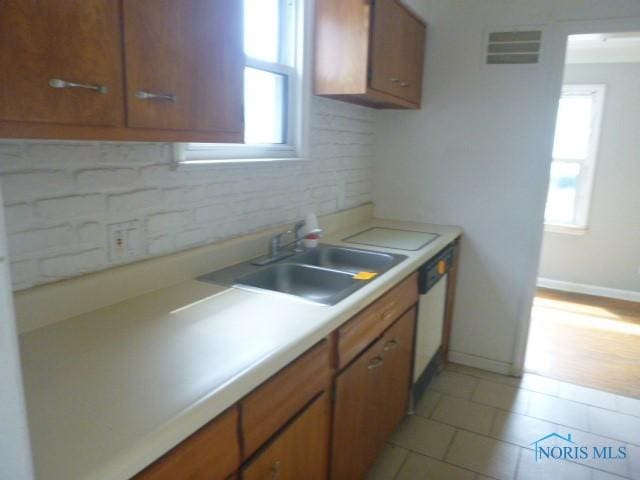 kitchen featuring light tile patterned floors, visible vents, brown cabinets, and a sink