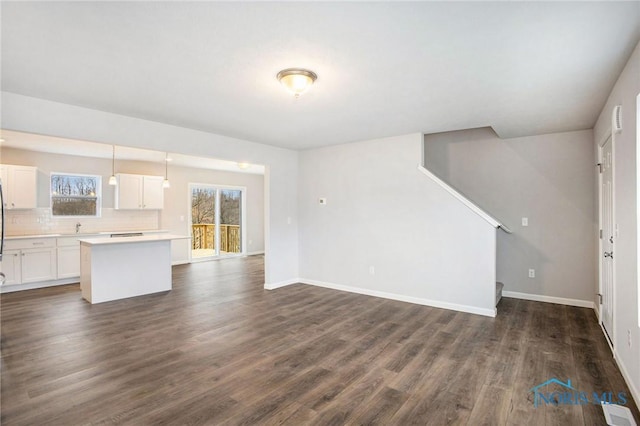 unfurnished living room with dark wood-style flooring, baseboards, visible vents, and a sink