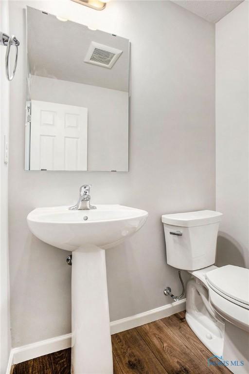 half bath featuring toilet, baseboards, visible vents, and wood finished floors