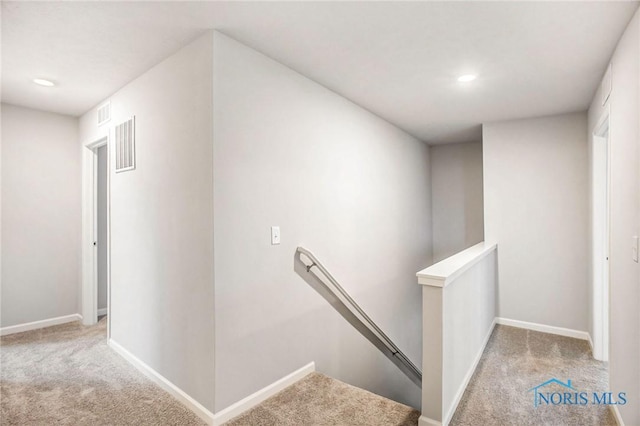 hall featuring carpet floors, baseboards, visible vents, and an upstairs landing