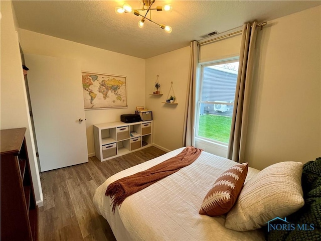bedroom with wood finished floors, an inviting chandelier, baseboards, visible vents, and a textured ceiling
