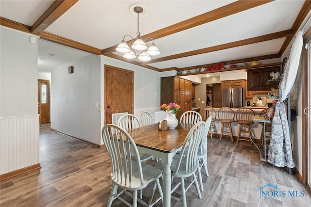 dining room featuring light wood-style floors, wainscoting, beam ceiling, and a notable chandelier