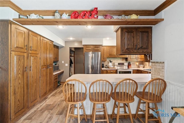 kitchen with stainless steel appliances, a kitchen bar, light wood finished floors, and a peninsula