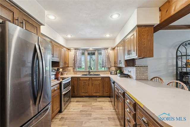 kitchen featuring backsplash, a sink, light countertops, stainless steel appliances, and light wood-style flooring