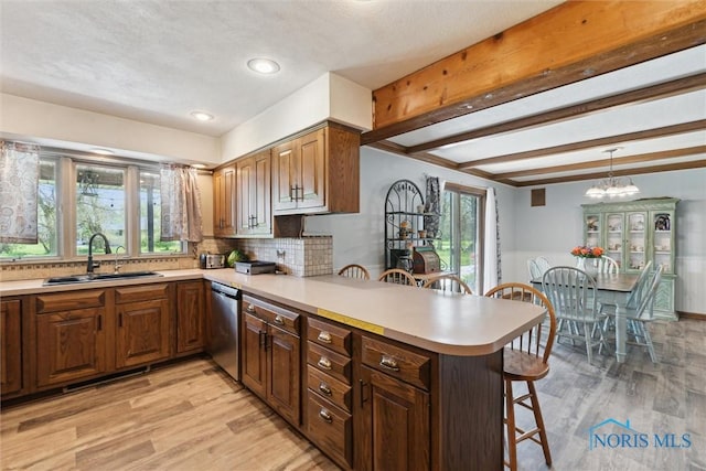 kitchen with a peninsula, a breakfast bar, light countertops, a sink, and dishwasher