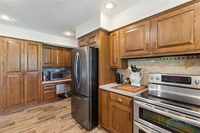 kitchen with brown cabinets, appliances with stainless steel finishes, decorative backsplash, and light countertops