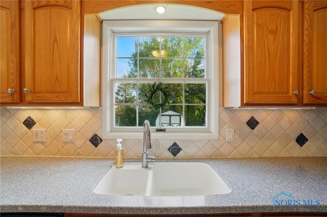 kitchen with a sink, light stone counters, decorative backsplash, and brown cabinets