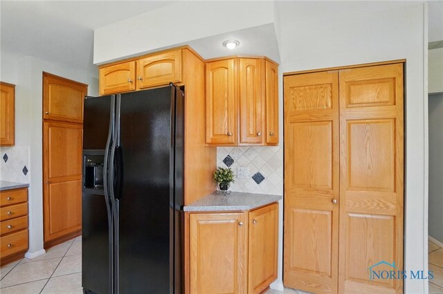 kitchen featuring light tile patterned floors, light stone countertops, backsplash, and black refrigerator with ice dispenser