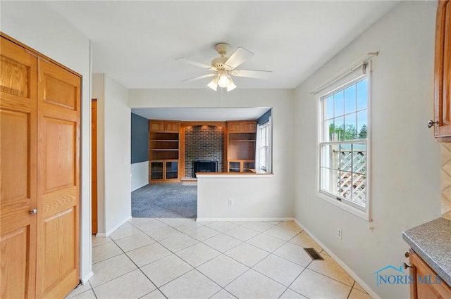 interior space with ceiling fan, visible vents, a brick fireplace, baseboards, and light tile patterned flooring