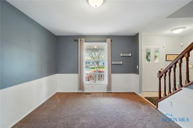 carpeted foyer with baseboards, visible vents, and stairway